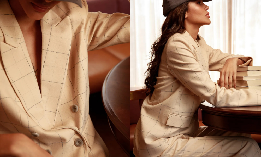 Modelo usando blazer feminino no outono estampa xadrez, em close e plano lateral, ajustando ou apoiando a postura enquanto se senta em um ambiente interno com luz quente.