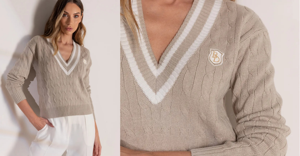 Look premium com tricot básico bege em ponto trançado, gola V com acabamento branco e detalhe de broche no peito. Modelo em foto editorial, usando com calça clara